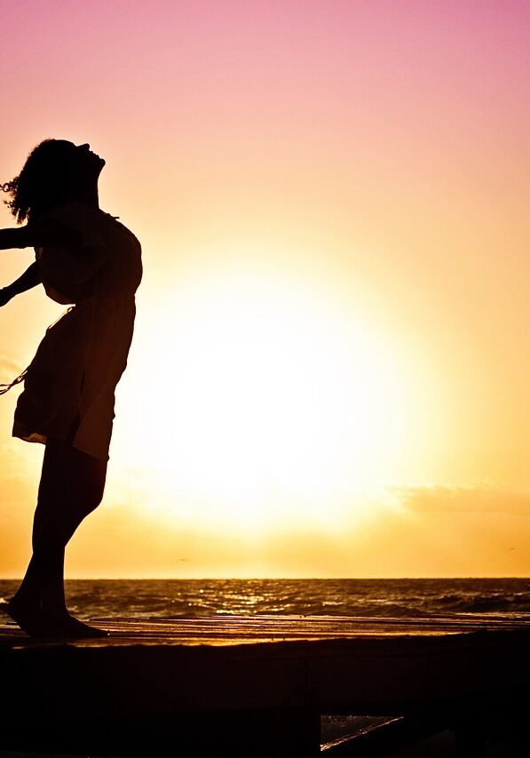 Silhouette of a woman at the beach with arms outstretched against a vibrant sunset backdrop.