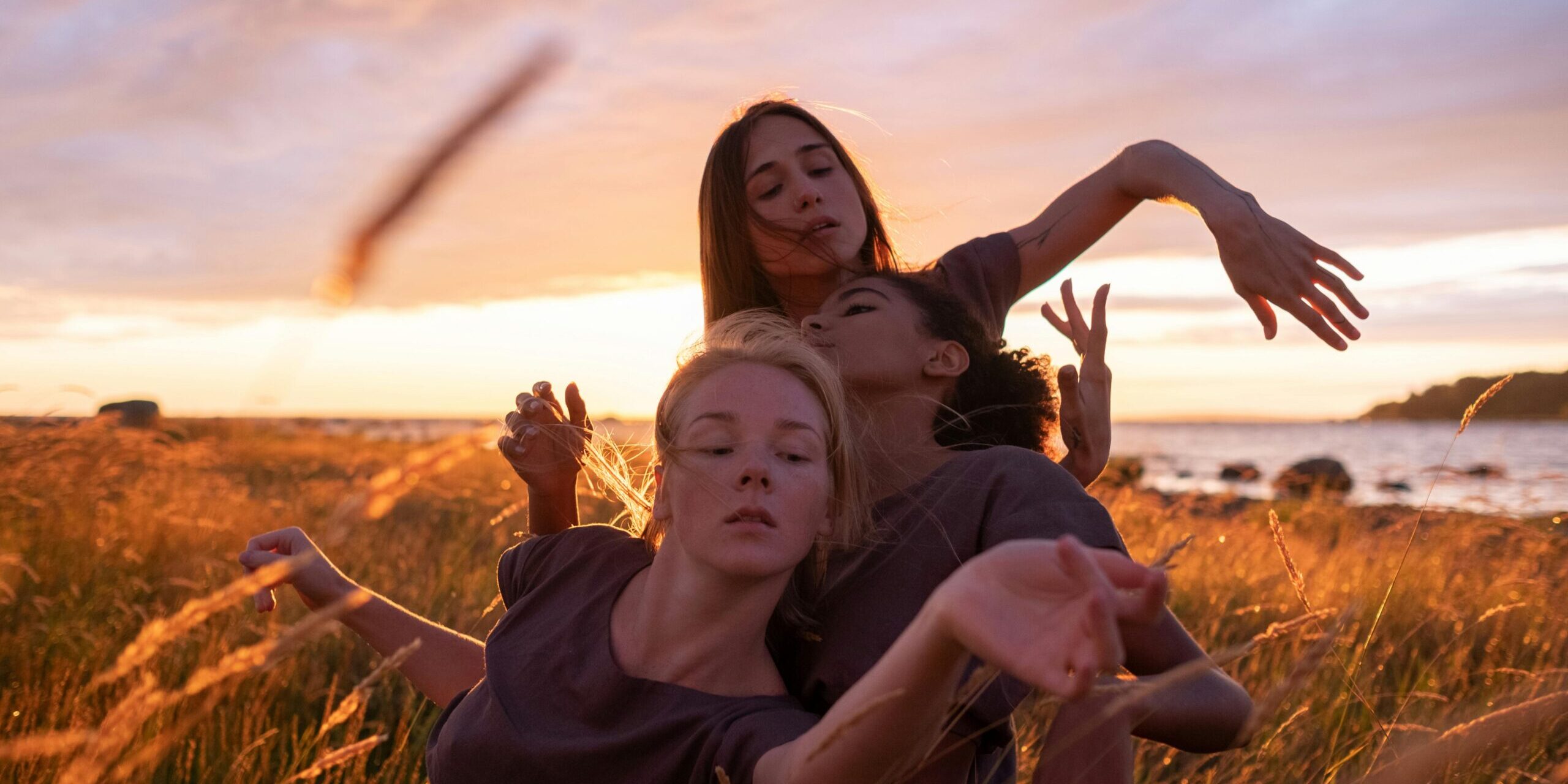 A group of women engaging in a graceful dance in a sunlit grass field during sunset.